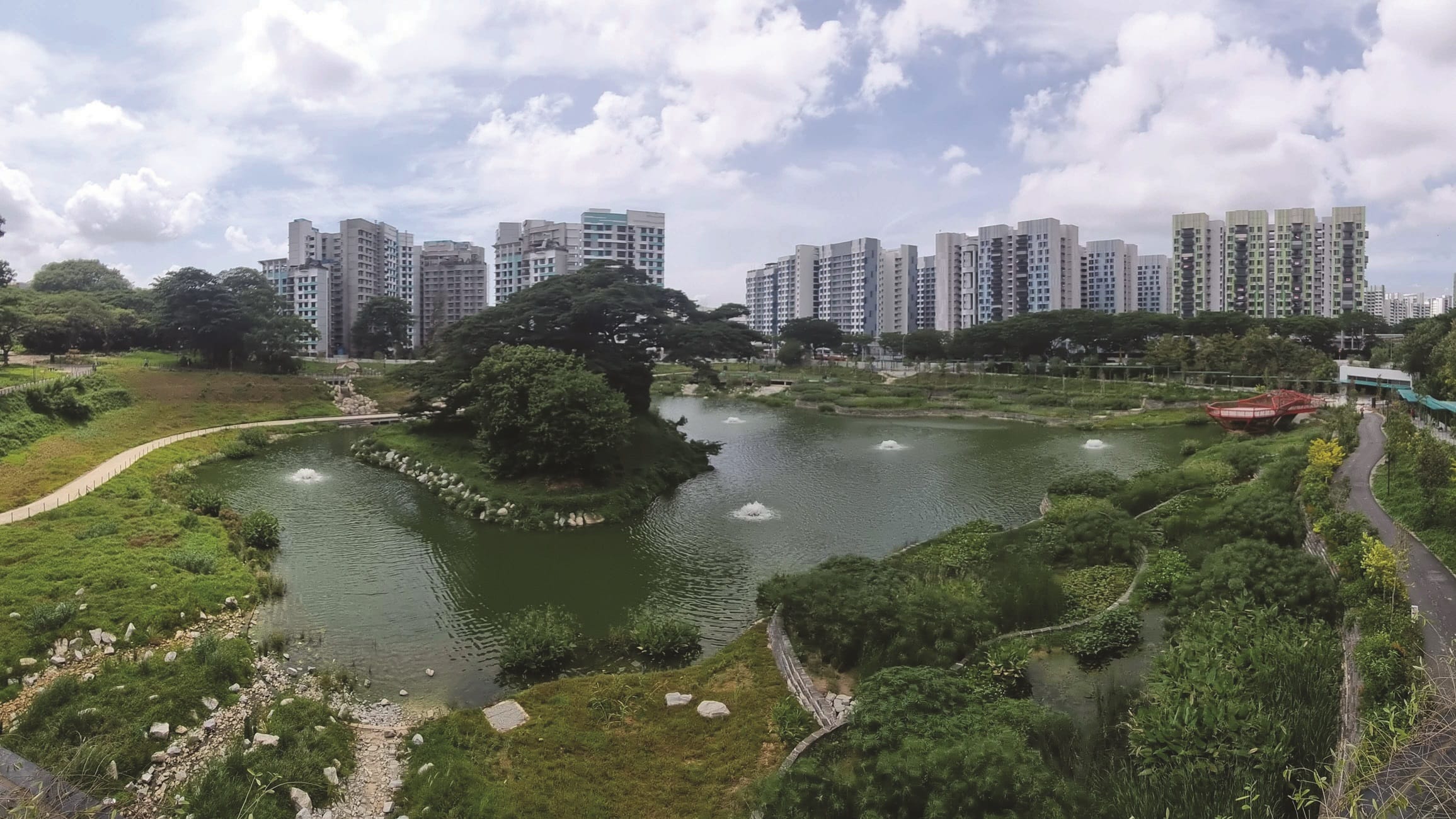 A park with a pond and walking paths in front of apartment buildings.